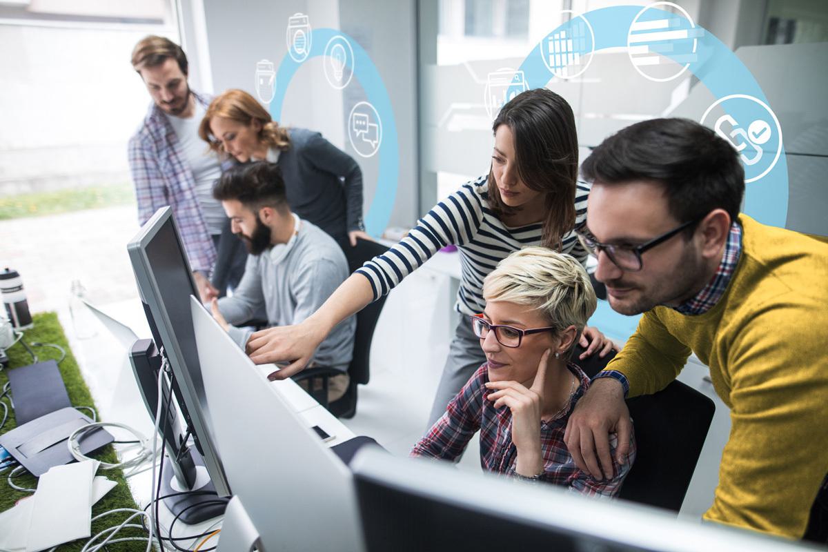 A group of coworkers smiling and clustered around a computer screen.